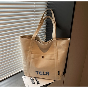 Détail du sac cabas en toile montrant la poche avant avec bouton en métal et broderie