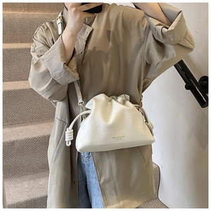 Close-up of white drawstring bucket bag with litchi texture and gold metal accents
