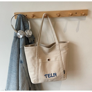 Détail du sac fourre-tout en toile beige avec poche avant et broderie TELN