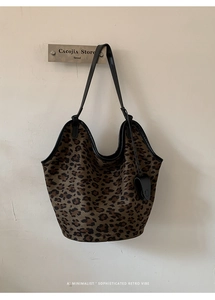 Détail du sac cabas imprimé léopard avec bordures noires et fines anses sur mur blanc