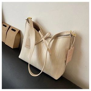 Vista dettagliata della borsa tote intrecciata crema con fiocco e tracolla sottile su sfondo
