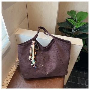 Détail du cabas en daim avec motifs d'étoiles en rivets et breloque à pompon coloré