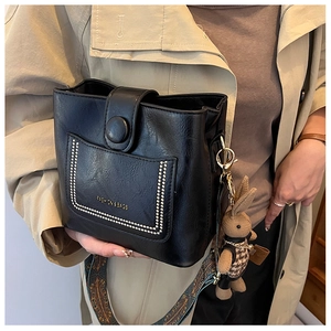 Detail of black faux leather bucket bag featuring a knit bunny charm and ethnic woven strap