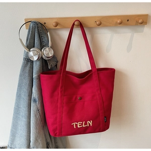 Détail du cabas en toile rouge avec poche avant à pression et lettrage TELN texturé