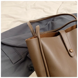 Détail d'un sac seau en cuir marron foncé mat avec poignées fines et bouton pression