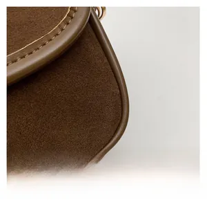 Detailed macro view of dark brown suede and smooth leather stitching on the shoulder bag