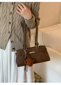 Detail shot of brown retro bucket bag with gold hardware and plush bear charm on beige sweater