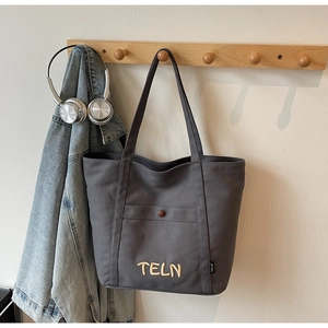 Détail du sac fourre-tout en toile gris foncé avec broderie jaune et poche à bouton avant