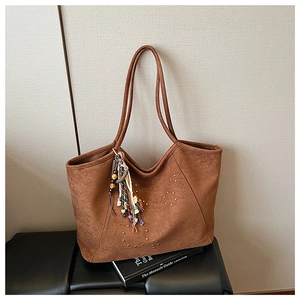 Détail du sac cabas en daim marron avec rivets métalliques et breloque à pompon tissé