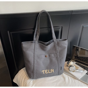 Détail du grand sac cabas en toile grise avec poche à bouton pression et broderie jaune