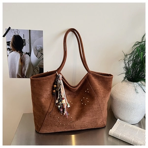 Détail d'un sac cabas en daim marron avec clous métalliques et pompon décoratif