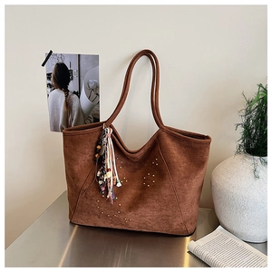 Détail d'un sac cabas en daim marron avec rivets dorés et pompon coloré bohème