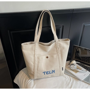 Détail du sac fourre-tout en toile blanc cassé avec broderie bleu marine et poche à bouton