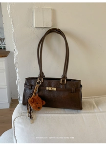 Detail of dark brown leather shoulder bag with gold buckle and a cute teddy bear charm