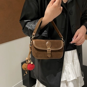 Brown suede shoulder bag detail featuring vintage flap design and plush pompom accessory