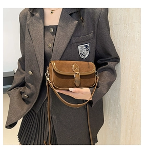 Detail of a brown suede crossbody bag with gold buckle on a gray blazer outfit