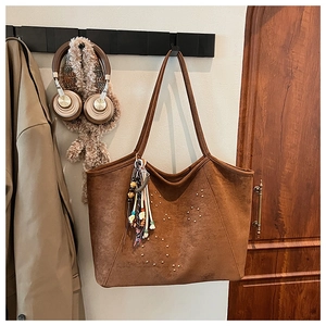 Gros plan d'un sac cabas en daim marron avec rivets dorés et breloque pompon en perles