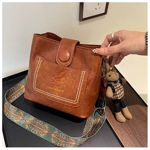 Close-up of brown bucket bag with rivet pocket and colorful geometric woven strap