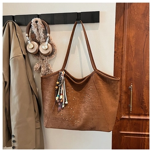 Détail d'un sac cabas en daim marron avec clous dorés et breloque pompon bohème