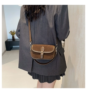 Detail of a vintage dark brown suede saddle bag worn over a grey blazer for daily styling