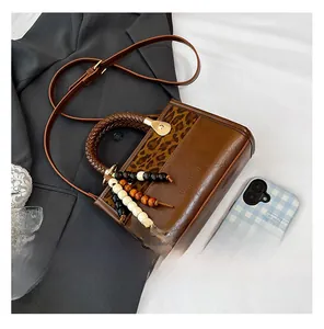Détail du sac en cuir marron avec panneau léopard, poignée tissée et breloque en bois