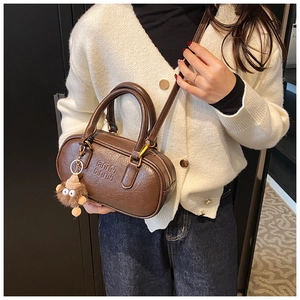 Close-up of brown embossed barrel bag with plush monkey charm and metal zip detail