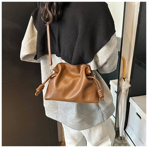 Close-up of brown drawstring leather bucket bag with textured finish and gold logo detail