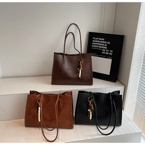 Three minimalist tote bags in dark brown, light tan, and black with beaded charms