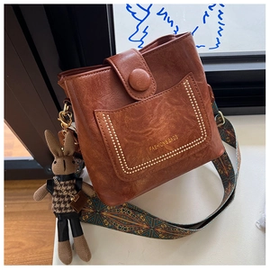 Brown leather bucket bag detail with colorful strap and rabbit charm on windowsill