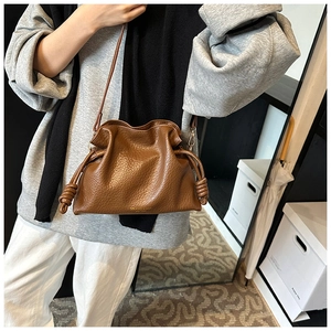 Close-up of brown ruched cloud bucket bag featuring drawstring closure and gold brand logo