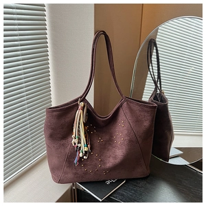 Détail d'un grand sac cabas en daim marron avec rivets et pendentif pompon bohème
