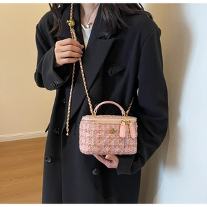 Pink tweed crossbody bag with gold chain strap worn over a black wool coat