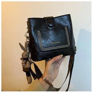 Detail of black PU leather bucket bag with gold rivets and wide patterned shoulder strap