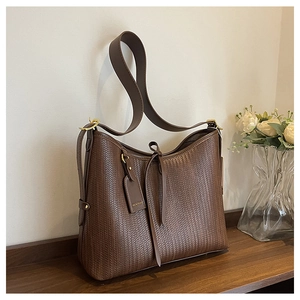 Dettaglio borsa tote marrone intrecciata con fibbia dorata e fiocco in pelle su ripiano