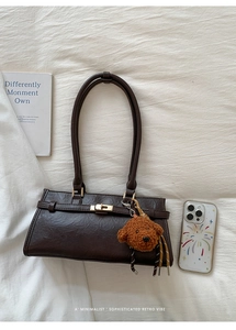 Detail view of a retro dark brown shoulder bag with a teddy bear charm on white fabric