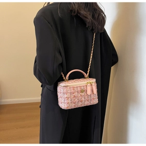Pink tweed vanity box bag with gold chain strap worn over a long black winter coat