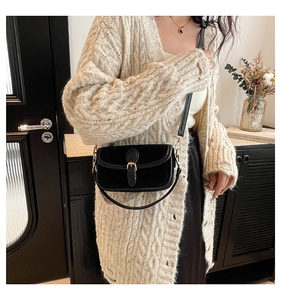 Close-up of black matte flap crossbody bag featuring a golden buckle and leather strap