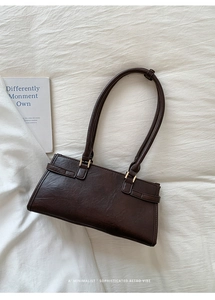 Detail of dark brown vintage leather shoulder bag with gold hardware on white fabric
