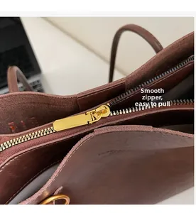 Detailed close-up of smooth gold metal zipper on a dark brown leather tote bag