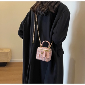 Pink tweed vanity bag with gold flower detail and chain strap shown on a black coat