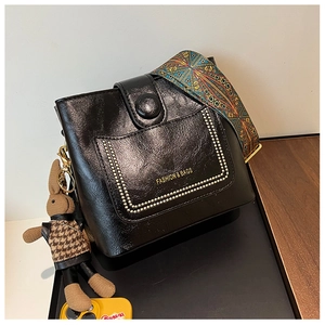 Detail of black glossy leather crossbody bag with ethnic patterned strap and rabbit charm