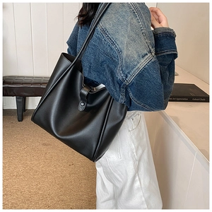 Détail d'un grand sac cabas noir avec bandoulière porté par un mannequin en intérieur