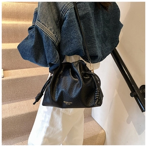 Close-up of black lychee leather bucket bag with gold lettering and drawstring detail