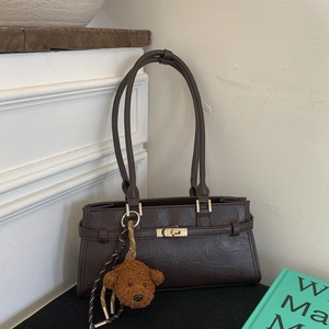 Detail of dark brown leather shoulder bag with gold clasp and plush bear charm