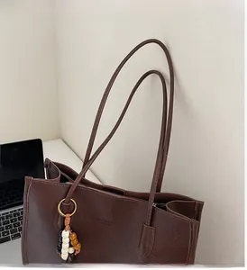 Detail of a brown leather tote bag with wooden bead charm and gold fashion lettering