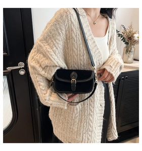 Detail of black velvet shoulder bag with golden buckle and textured flap closure