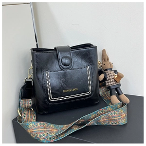 Detail of black leather bucket bag featuring ethnic strap and plush rabbit charm
