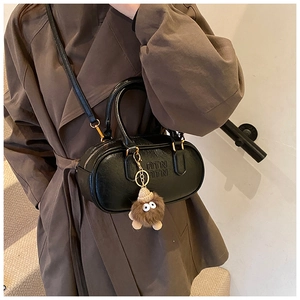 Chic black bowling bag with top handles, crossbody strap, and plush charm decoration