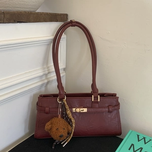 Detail of burgundy vintage shoulder bag featuring gold twist lock and cute dog plush charm