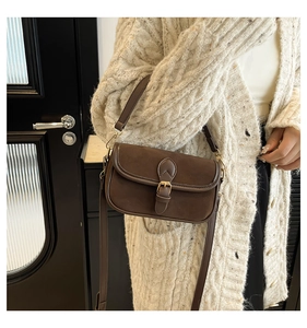 Close-up of vintage brown suede crossbody bag with heart buckle on a white knit cardigan
